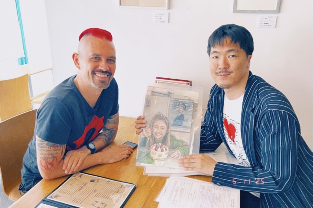 左側にダミアンさん、右側に風間が刑務所アート展の応募作品を持っている。